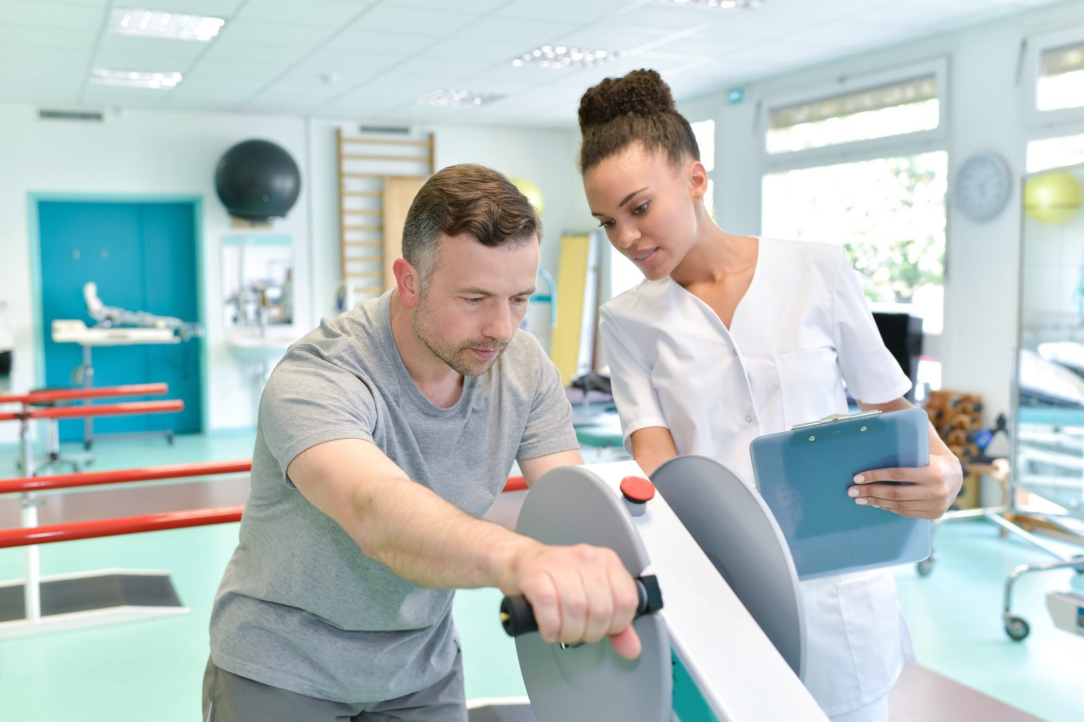 A man exercises on a rehabilitation machine while a physical therapist watches, when needing long term care and meeting with Suffolk car accident lawyer to handle injury case.